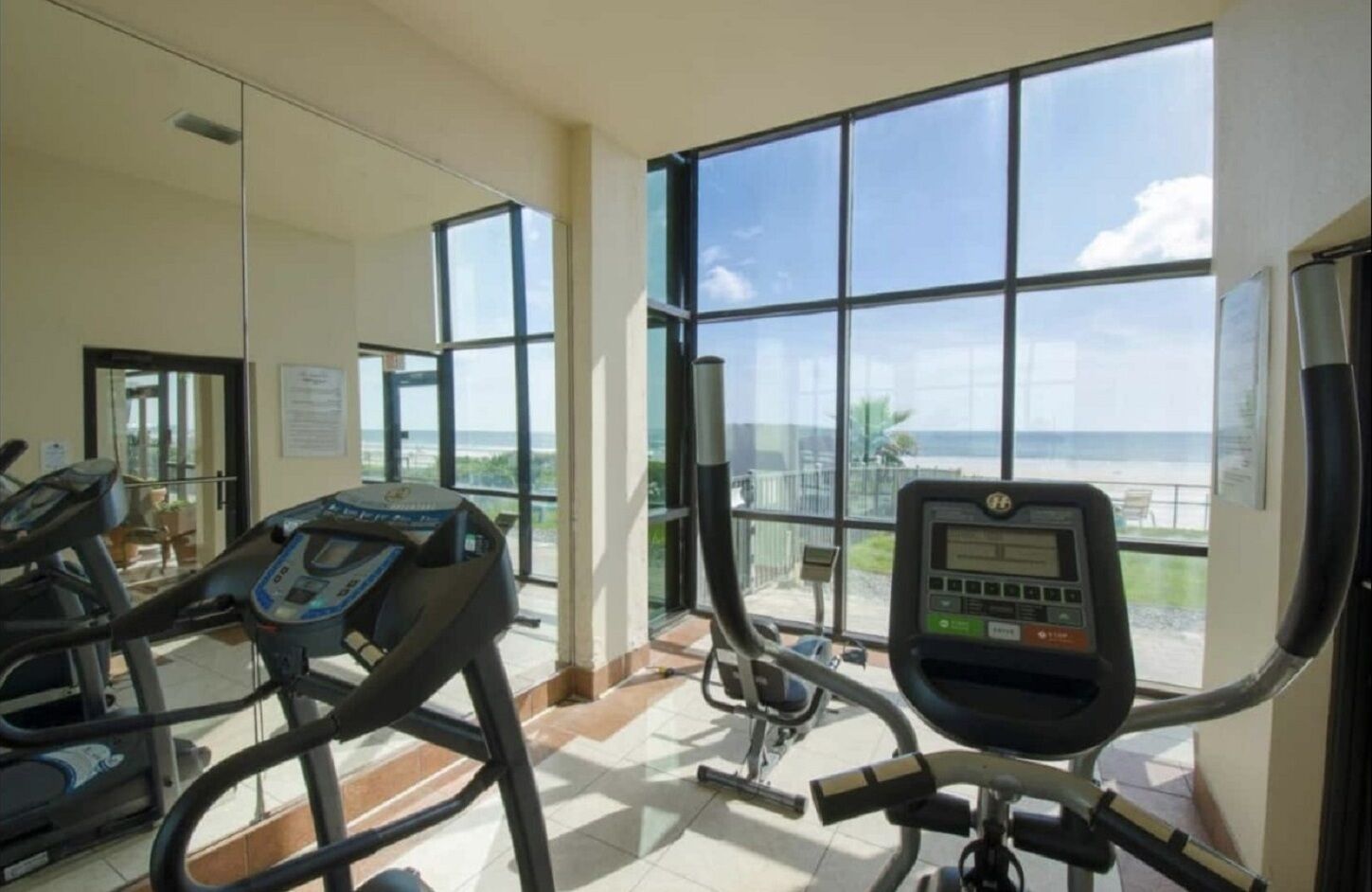 Ein Fitnessstudio mit Laufbändern und Trainingsgeräten, große Fenster mit Meerblick.