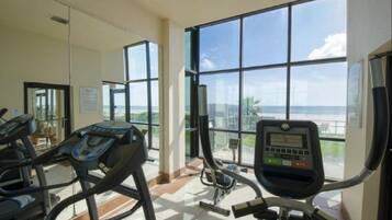 Ein Fitnessstudio mit Laufbändern und Trainingsgeräten, große Fenster mit Meerblick.