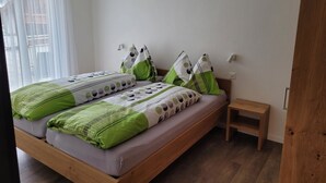 Una camera da letto con un letto di legno, biancheria verde e bianca, un comodino e una finestra con tende leggere.