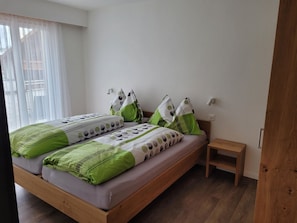 A bedroom with a wooden bed, green and white bedding, a small bedside table, and a window with sheer curtains. - Haus Perle Appartement/Fewo 3-Bettwohnung Nr. 2 by Interhome (Saas-Fee)