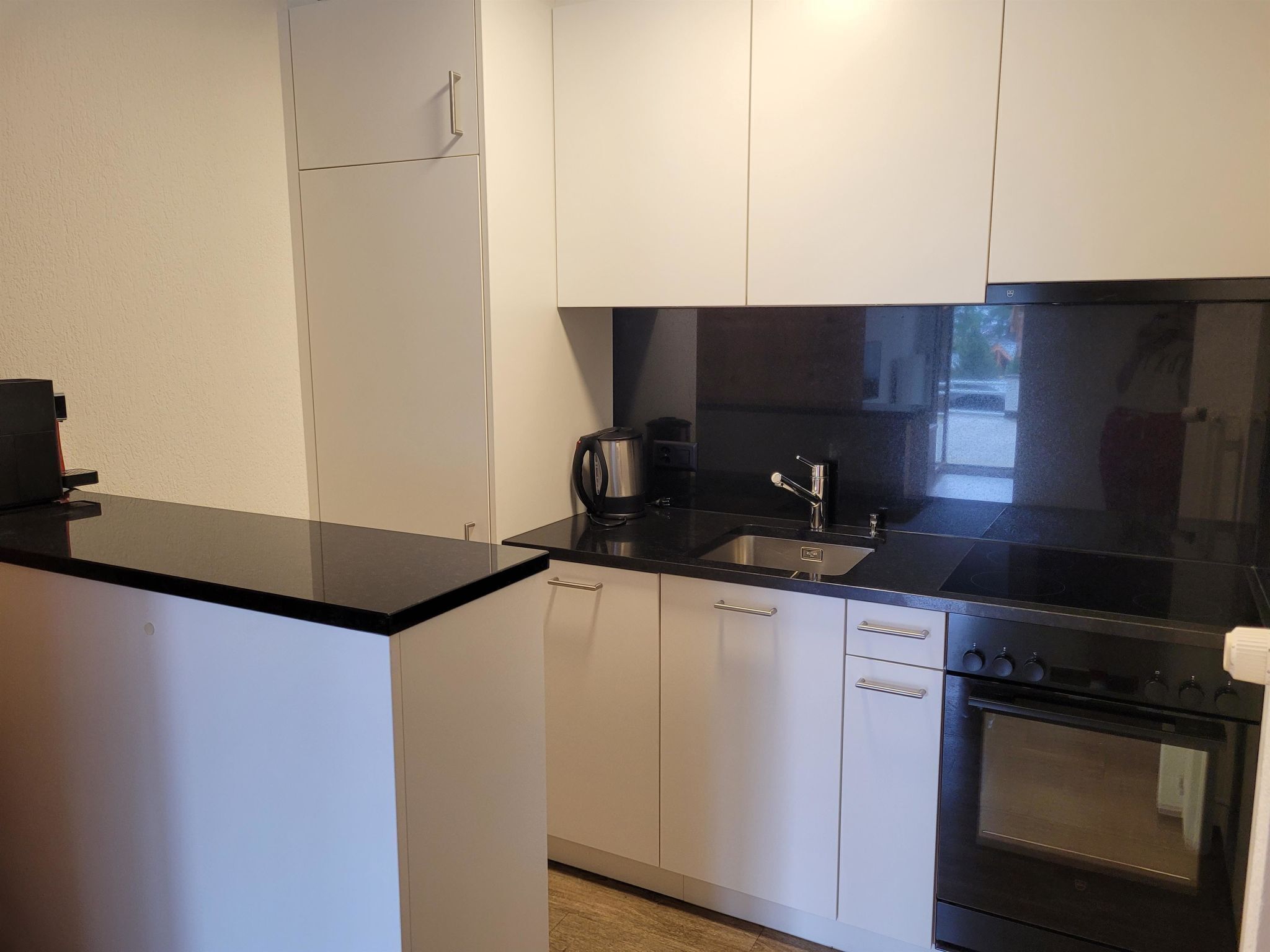 A compact kitchen with white cabinets, a black countertop, a stainless steel sink, and a built-in oven.