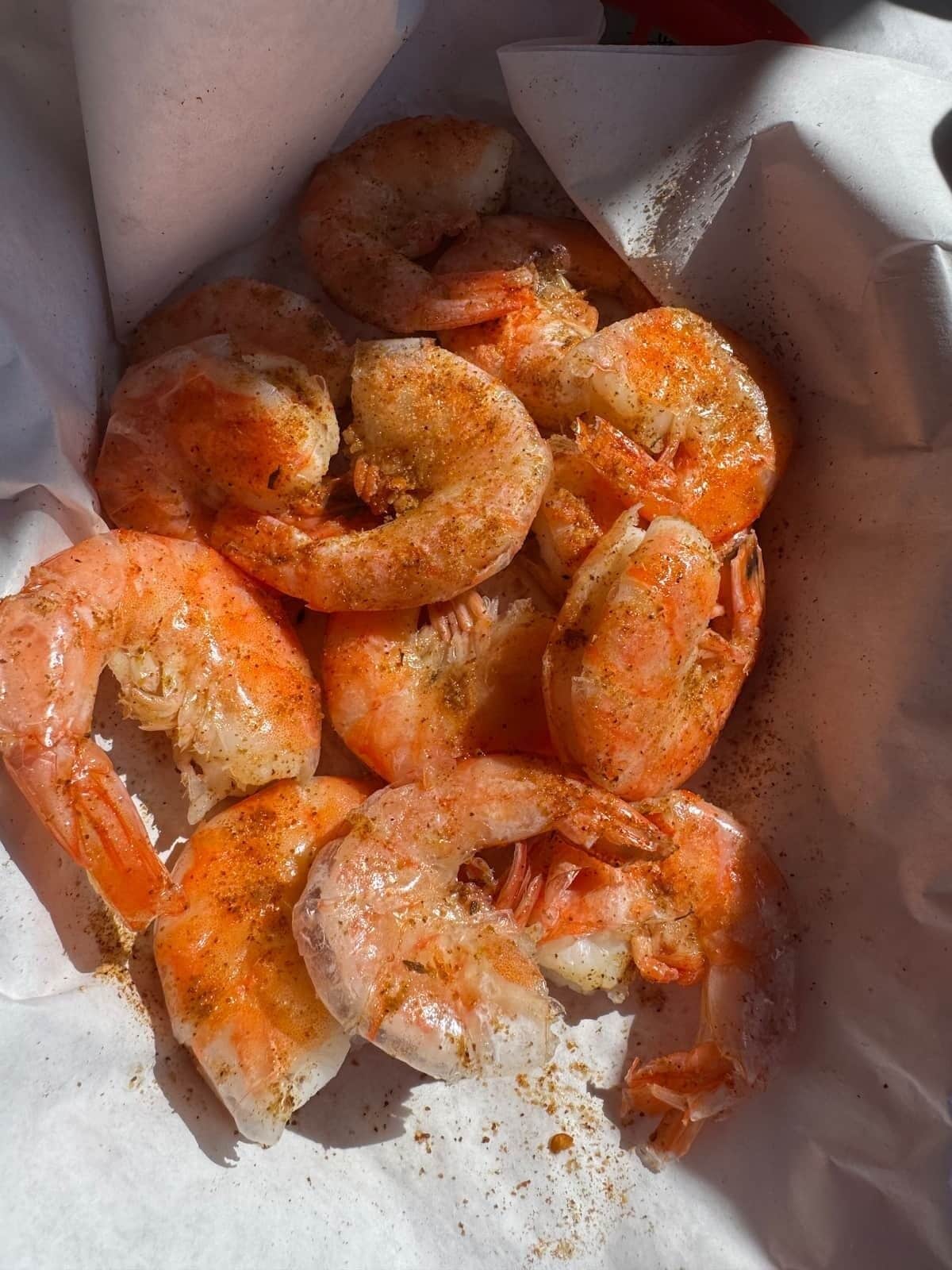 A container of cooked shrimp seasoned with spices.