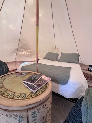 A tent with a bed, a table with a book, and a decorative stool.