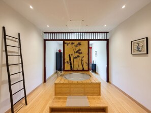 Een kamer met een houten vloer, een badkuip, een ladder, een decoratieve wand en een ingelijst kunstwerk.