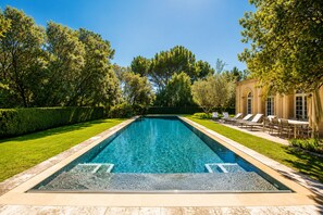 Ein rechteckiger Swimmingpool mit glasklar blauem Wasser, umgeben von einem gepflegten Rasen und Bäumen.