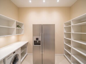 Eine moderne Küche mit einem eingebauten Edelstahlkühlschrank, einer Waschmaschine und viel Stauraum durch weiße Regale.