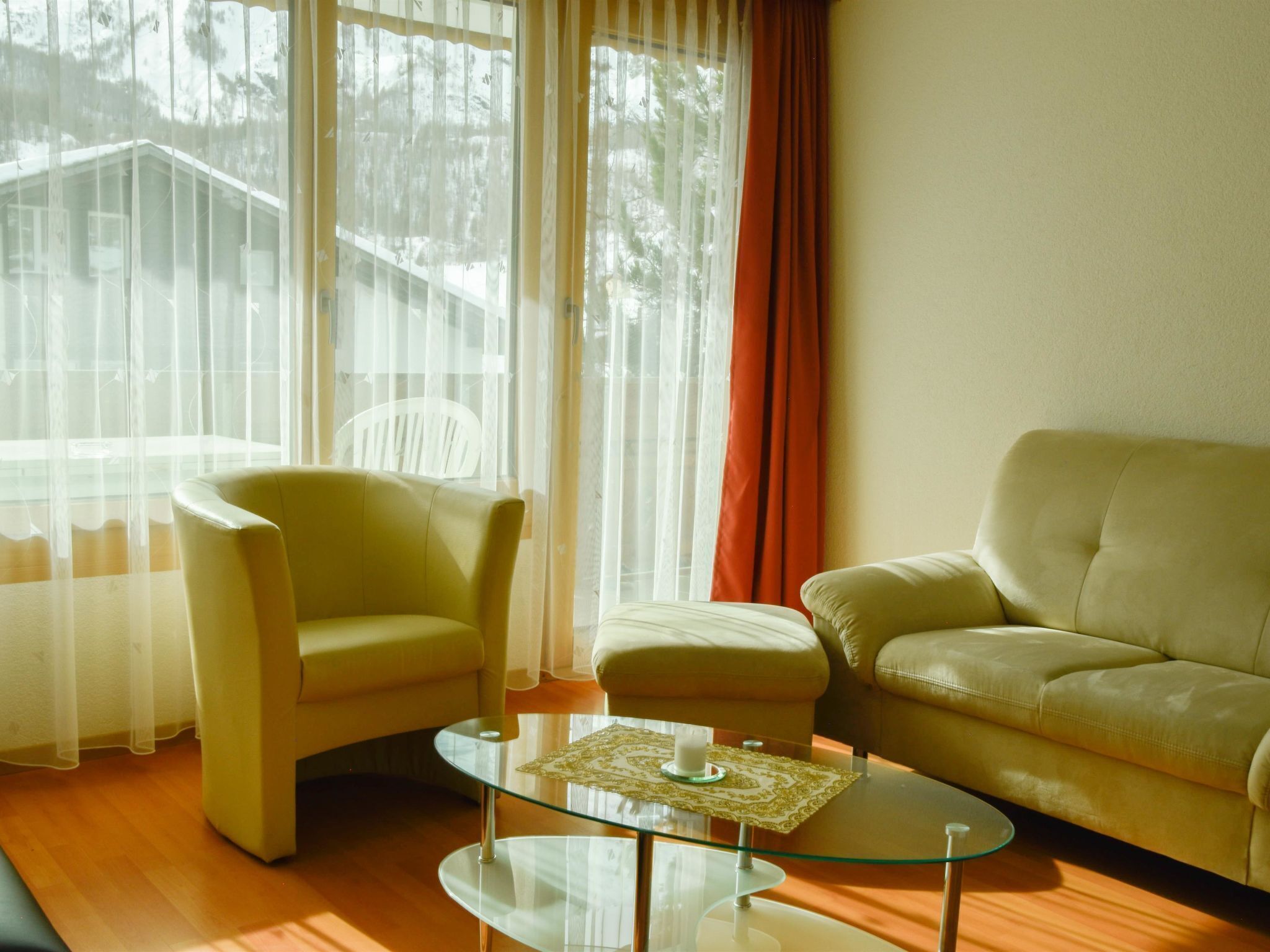 A living room with a glass coffee table, two armchairs, and a sofa.