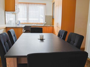 A dining area with a table and chairs, a kitchen in the background, and a window with curtains. - Heidi Appartement/Fewo 5-Bettwohnung Nr. 63 by Interhome (Saas-Fee)