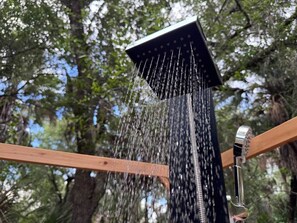 Eine Duschbrause, aus der Wasser fließt, vor einer Baumkulisse.