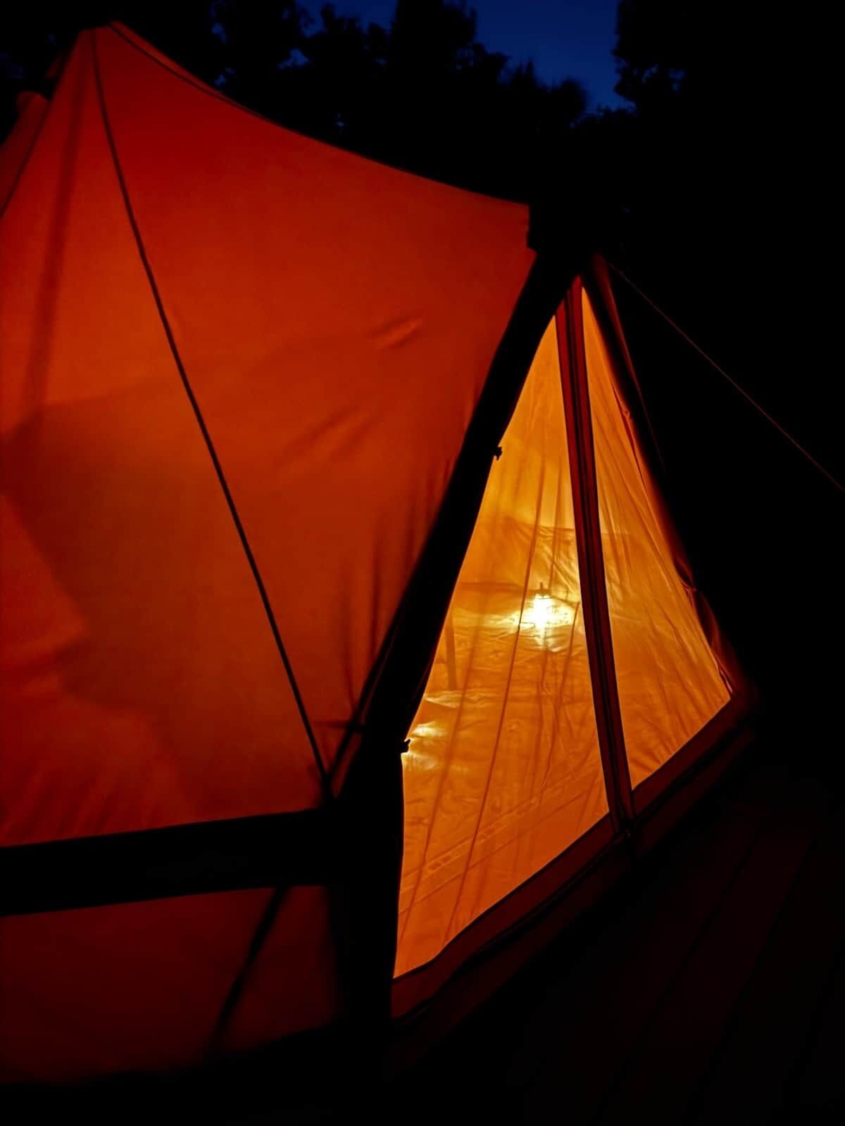 Une tente dotée d’une entrée triangulaire et d’une source de lumière visible à l’intérieur.