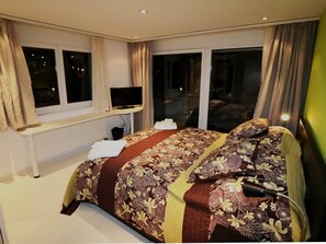 Hotellihuone, jossa on sänky, työpöytä tietokoneella ja ikkuna.