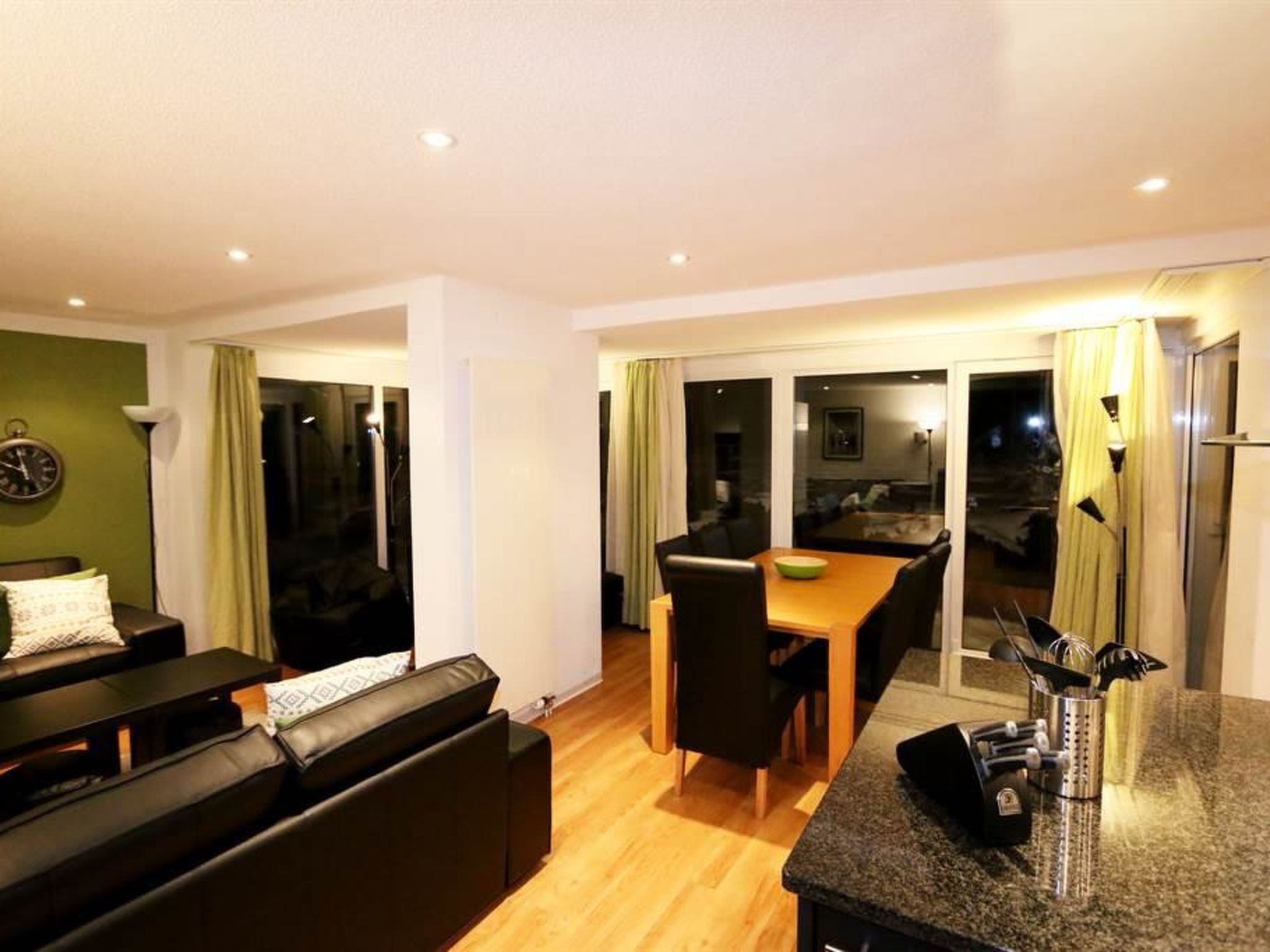 A modern living room with a sofa, a dining table with chairs, and a kitchen area with a countertop and utensils.