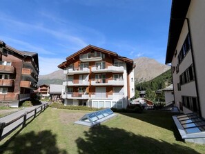 A multi-story residential building with balconies, a grassy courtyard, and a mountain in the background. - Nicoletta Appartement/Fewo 8-Bettwohnung by Interhome (Saas-Fee)
