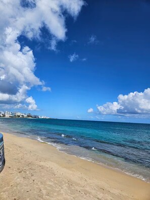 A beach with clear blue water and a city skyline in the distance. - Spacious 3BR steps to Beach- Family friendly (San Juan)
