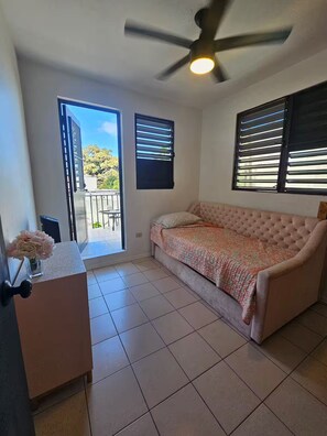 A room with a bed, a ceiling fan, a window with blinds, and a door. - Spacious 3BR steps to Beach- Family friendly (San Juan)