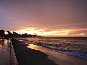 A sunset over a beach with a city skyline in the background. - Spacious 3BR steps to Beach- Family friendly (San Juan)