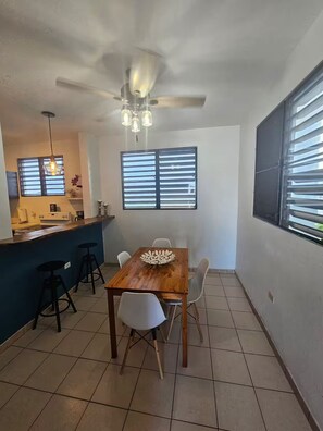 A dining area with a wooden table, white chairs, a ceiling fan, and a kitchen in the background. - Spacious 3BR steps to Beach- Family friendly (San Juan)