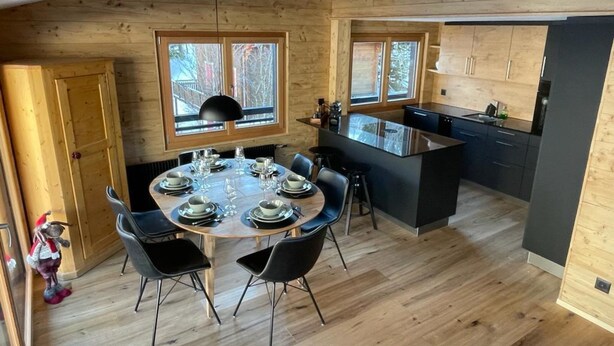 Una cocina moderna con paredes de madera, un comedor con una mesa redonda preparada para cuatro personas y ventanas amplias.