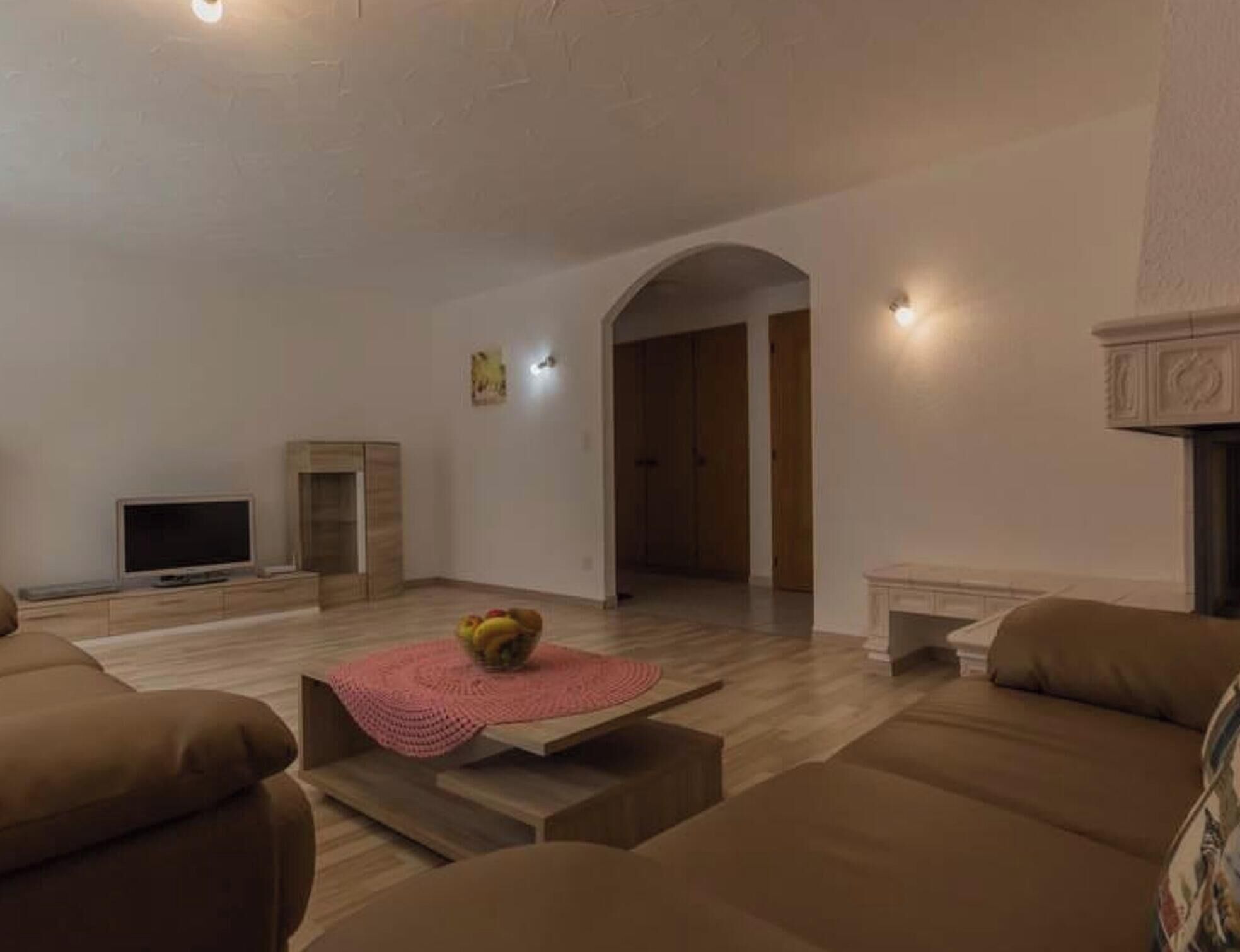 A living room with a television, a sofa, a coffee table with fruit, and a fireplace.