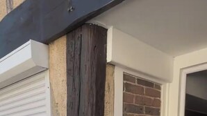 Eine Ziegelhausfassade mit einer weißen Tür, einem Fenster mit Rollläden und einem Verteilerkasten.