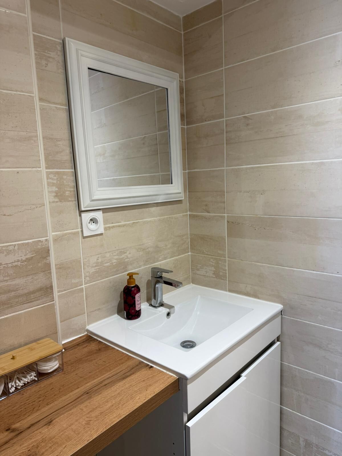A bathroom with a white sink, a mirror, and beige tiles.