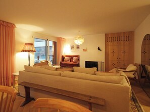A cozy living room with a sofa, a table, a lamp, and a window with curtains. - Sonnenhof Juliet Appartement/Fewo Appartement/Fewo by Interhome (Saas-Fee)