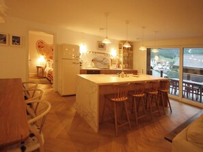 Eine moderne Küche mit Kochinsel, Barhocker und großem Fenster mit Blick auf eine Wohngegend.