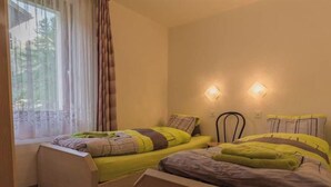 A bedroom with two beds, a window with curtains, and two wall-mounted lights. - Bergfink Appartement/Fewo 4-Bettwohnung Nr. 3 by Interhome (Saas-Fee)