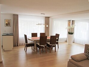 A modern dining area with a round table, six chairs, and a large window with curtains. - Adonis Appartement/Fewo, Dusche oder Bad, WC 4-Bettwohnung by Interhome (Saas-Fee)