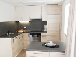A modern kitchen with light wood cabinets, a black countertop, and a coffee machine. - Adonis Appartement/Fewo, Dusche oder Bad, WC 4-Bettwohnung by Interhome (Saas-Fee)