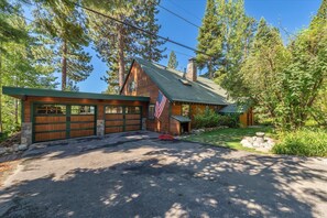 A wooden cabin with a garage, surrounded by trees and a stone pathway. - Tahoe Vista Getaway: Lake View & Hot Tub & Deck (Tahoe Vista)