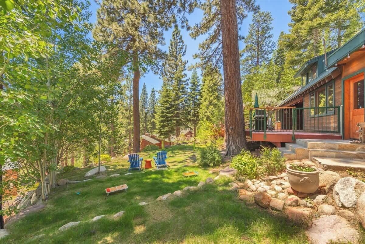 A cabin with a deck, surrounded by tall trees and a grassy yard.