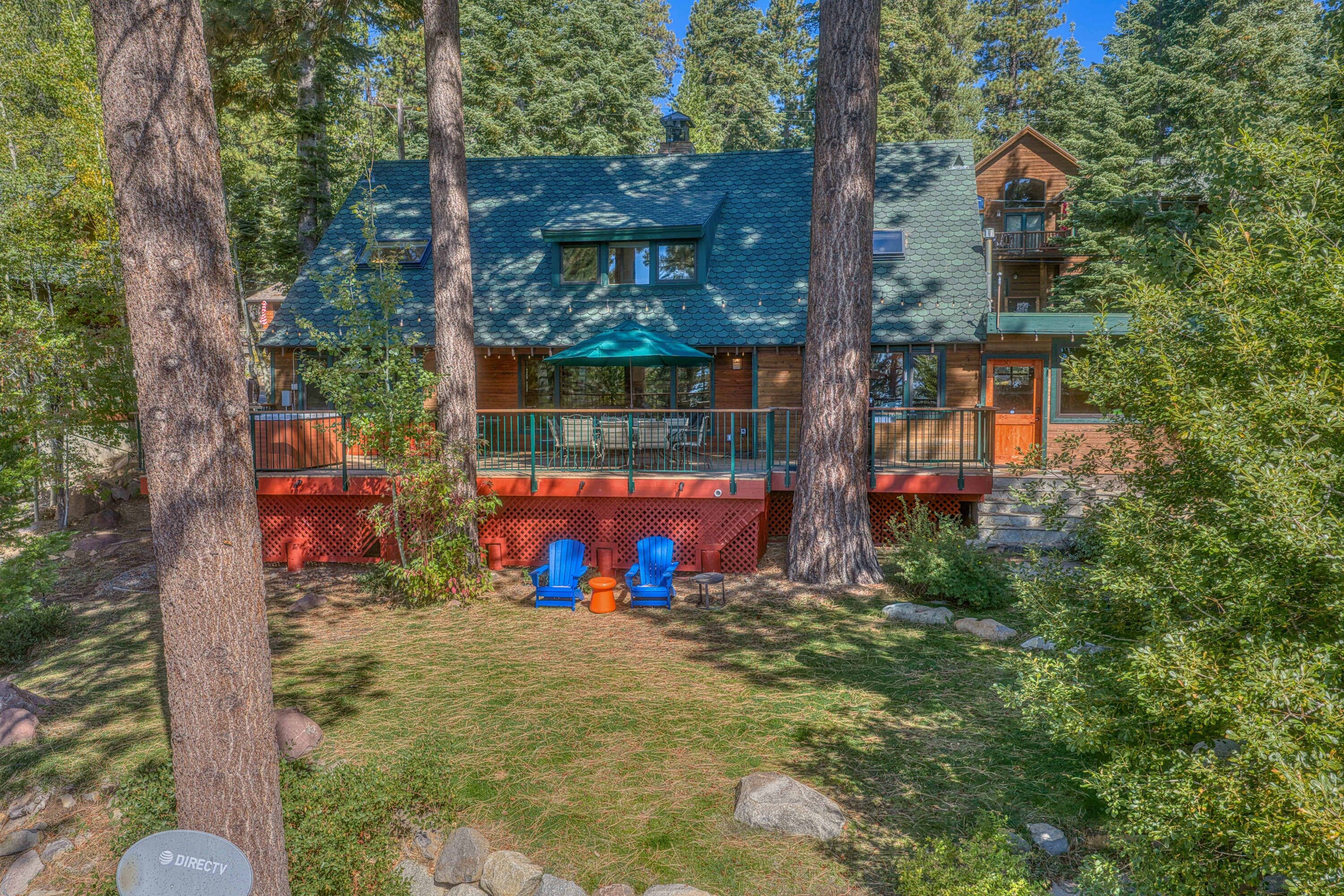 A cabin with a green roof, surrounded by trees, and featuring a deck with outdoor seating.