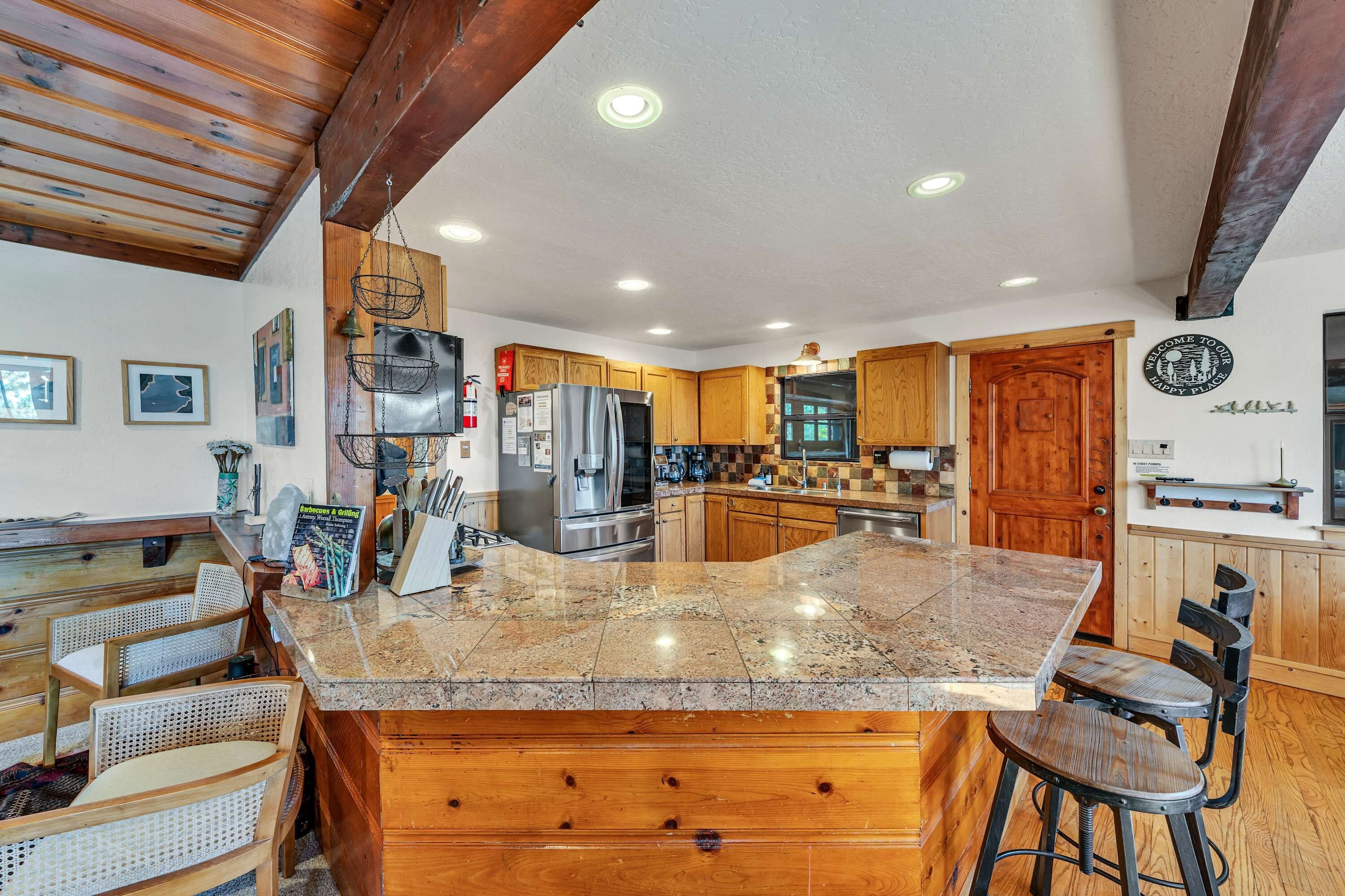 A spacious kitchen with a large granite island, wooden cabinets, and a dining area with rattan chairs.
