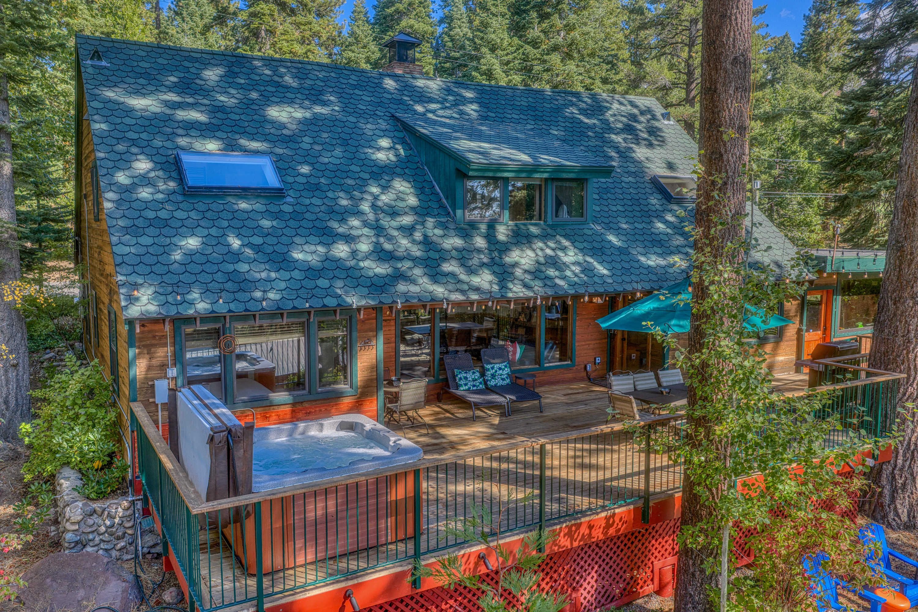 A cabin with a deck, hot tub, and outdoor seating area surrounded by trees.