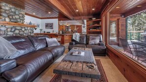 A cozy living room with a leather sofa, a coffee table, and a view of the outdoors through large windows. - Tahoe Vista Getaway: Lake View & Hot Tub & Deck (Tahoe Vista)