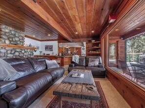 A cozy living room with a leather sofa, a coffee table, and a view of the outdoors through large windows. - Tahoe Vista Getaway: Lake View & Hot Tub & Deck (Tahoe Vista)