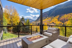 Une terrasse dotée d’un foyer extérieur, de mobilier de jardin et offrant une vue sur un paysage montagneux aux couleurs automnales.