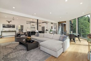 A modern living room with a sectional sofa, a coffee table, and a dining area with a glass table. - East Vail Retreat | Hot Tub, Fire Pit & Views (Vail)