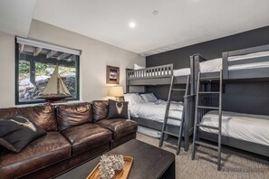 Ein kleines Zimmer mit Etagenbett, Ledersofa, einem Tisch und einem Fenster mit Blick auf ein Segelboot.