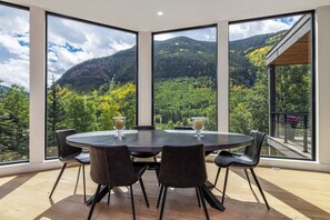 Un comedor con una mesa redonda y sillas, con ventanas amplias que ofrecen vistas a la montaña.