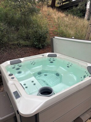 Ein Whirlpool mit Bedienfeld, umgeben von viel Grün und einer Holzterrasse.
