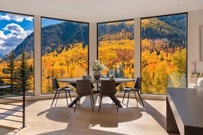 A dining area with a table and chairs, large windows with a mountain and autumn foliage view. - East Vail Retreat | Hot Tub, Fire Pit & Views (Vail)