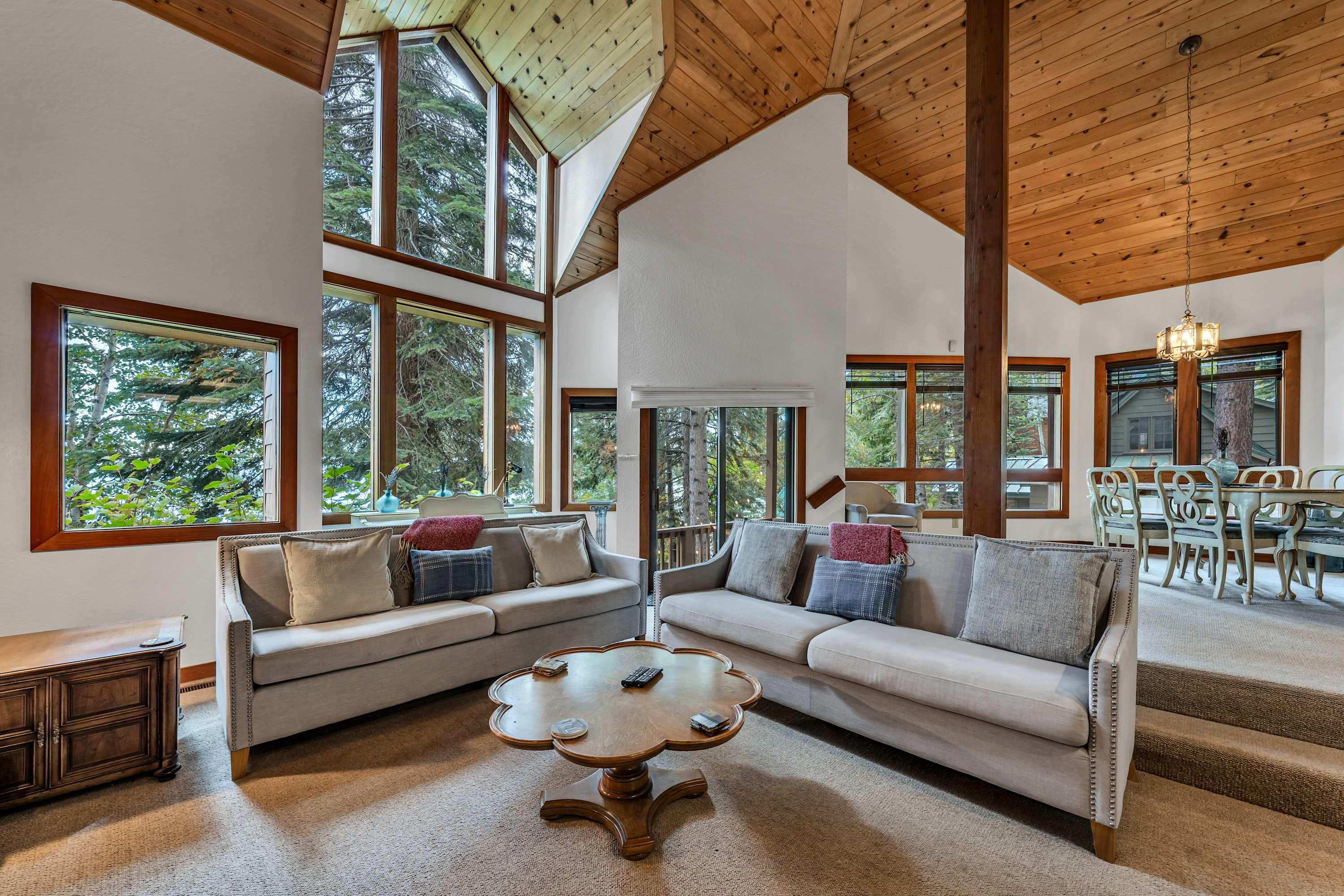 A spacious living room with high ceilings and large windows, a cozy seating area with a coffee table, and a dining area with a chandelier.
