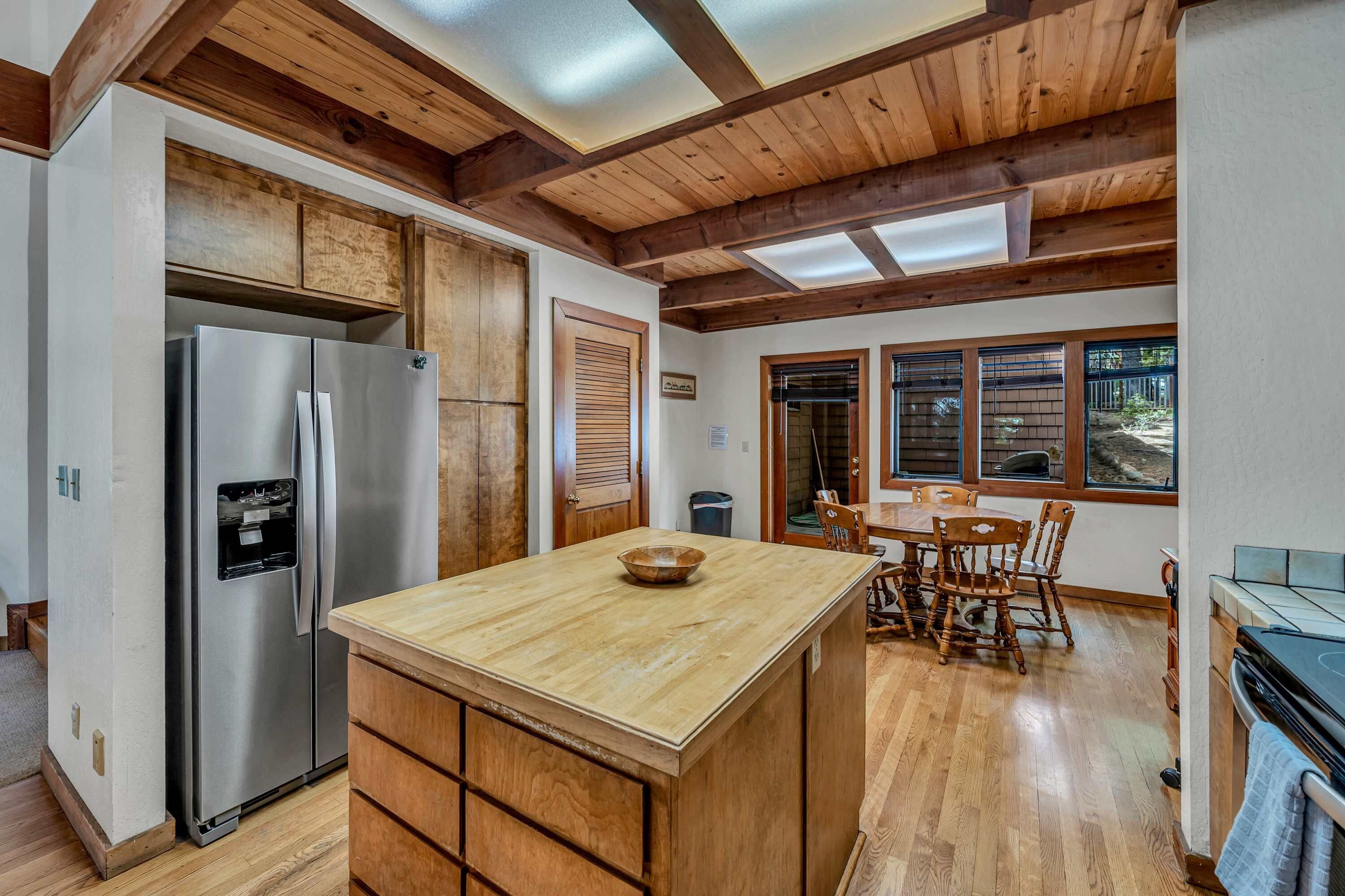 Una cocina con armarios de madera, un refrigerador de acero inoxidable, una isla de madera y un comedor con mesa y sillas.