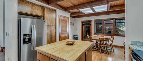 Una cocina con armarios de madera, un refrigerador de acero inoxidable, una isla de madera y un comedor con mesa y sillas.