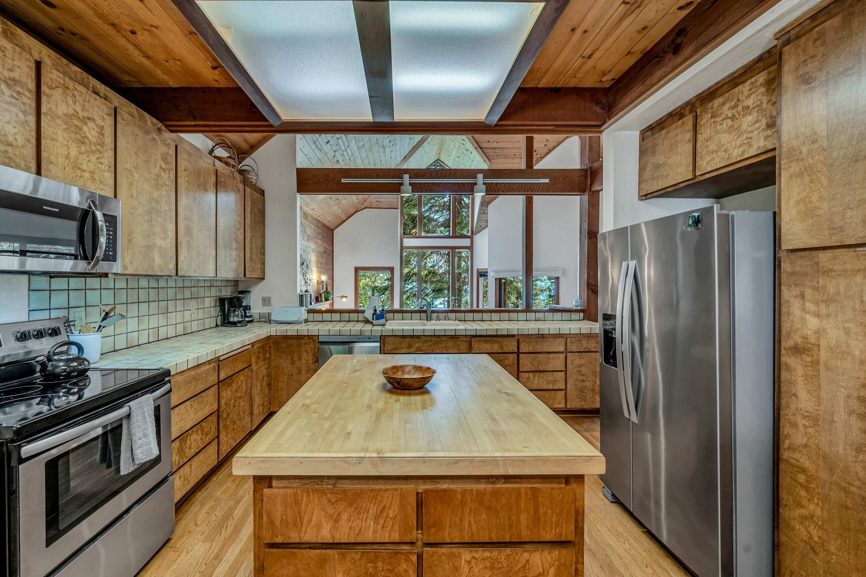 A modern kitchen with wooden cabinets, a stainless steel refrigerator, and a large island.