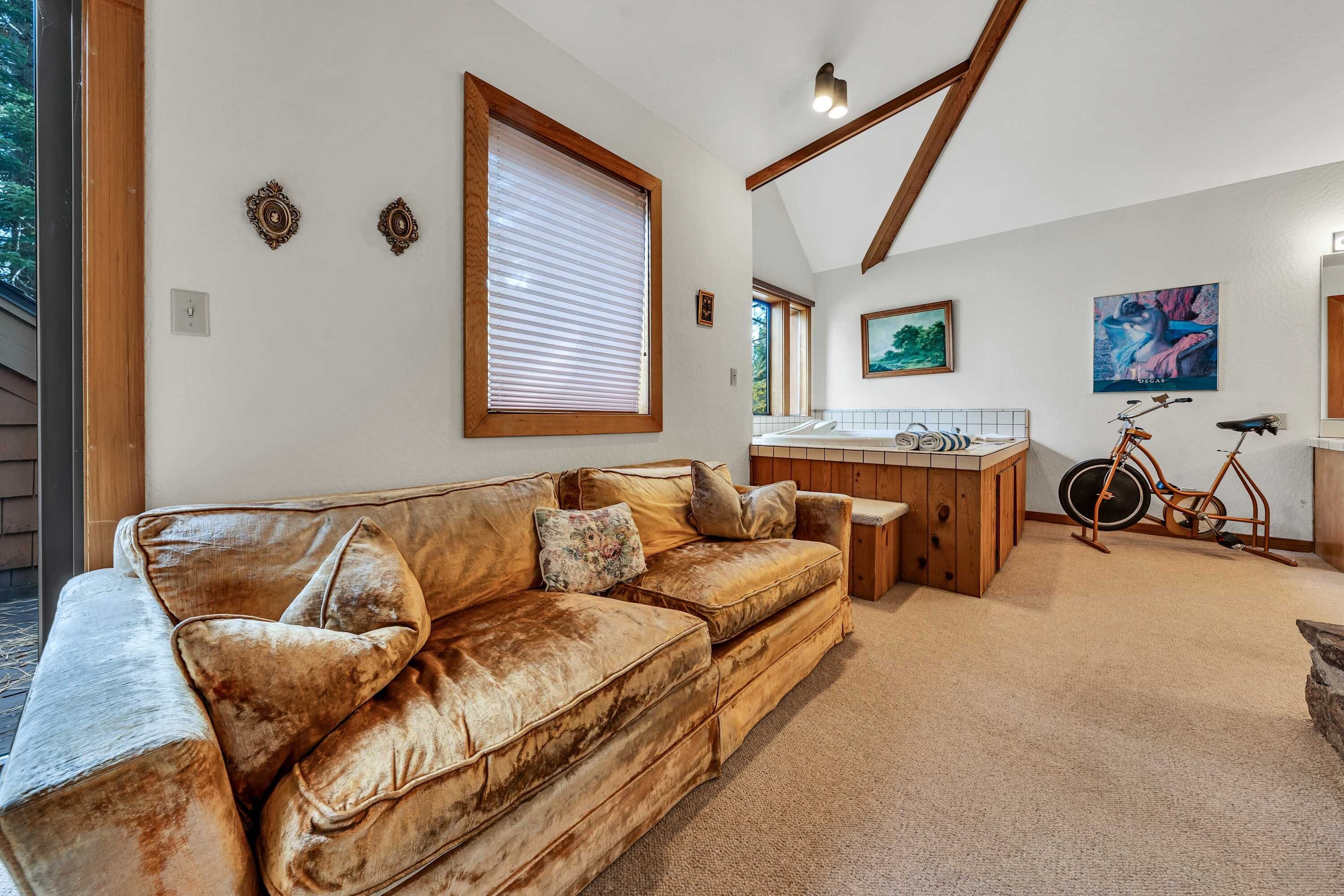 A cozy living area with a leather sofa, wooden beams, and a kitchen with a bicycle.
