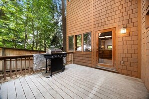 Eine Terrasse mit Grill, Holzboden und einem Backsteinhaus mit Glastür.