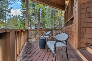 Une terrasse en bois avec deux fauteuils en osier et une table ronde, donnant sur une zone boisée.